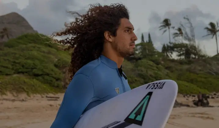 Surfista segurando prancha com logo Vissla e jaqueta neoprene Vissla na praia.