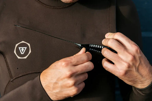 Imagem de surfista vestindo wetsuit Vissla marrom com logo da marca e zíper no peito.